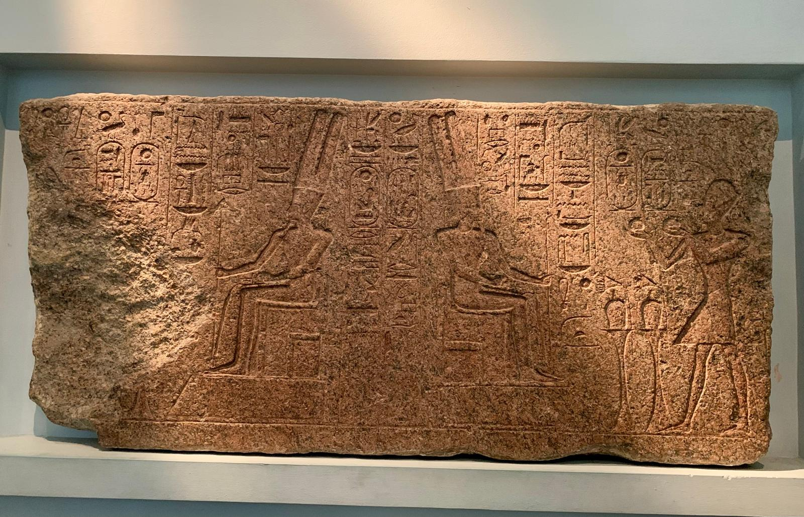 A granite block carved with hieroglyphs and two seated Egyptian gods receiving an offering.