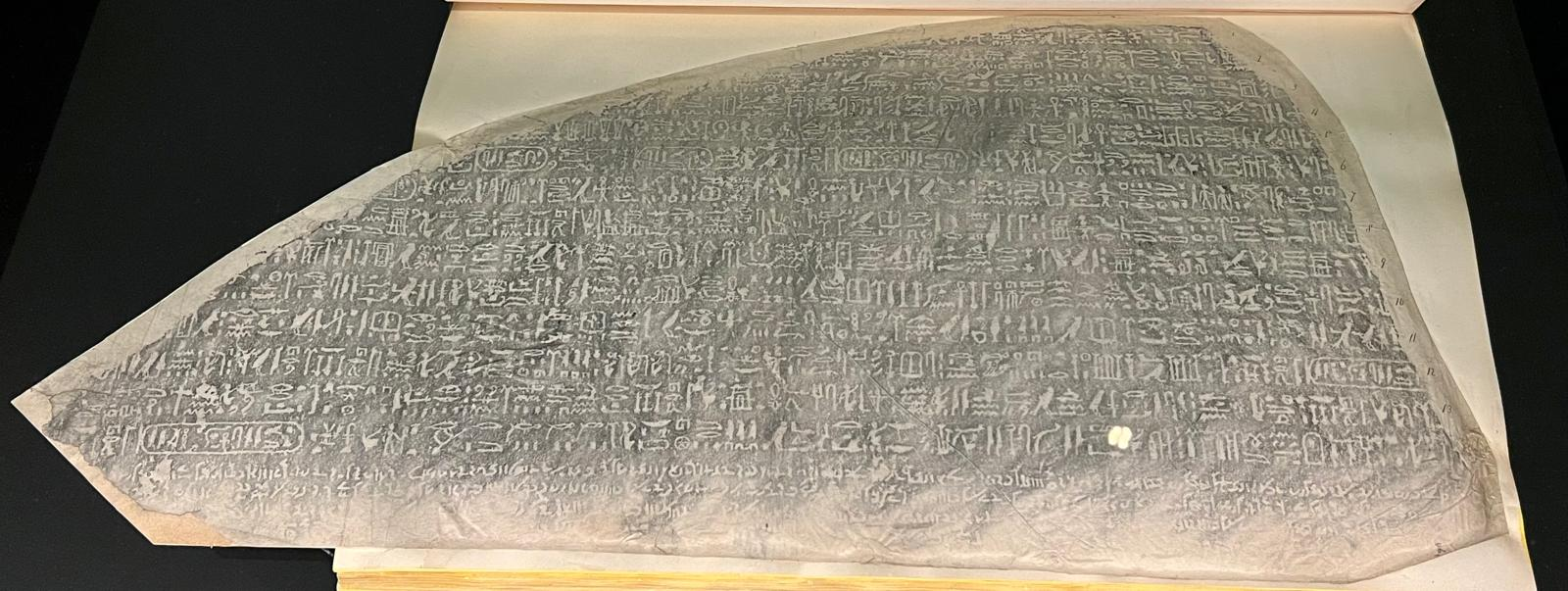 A print of the Rosetta Stone's inscription, hieroglyphs above and Demotic script below, laid open in a book.