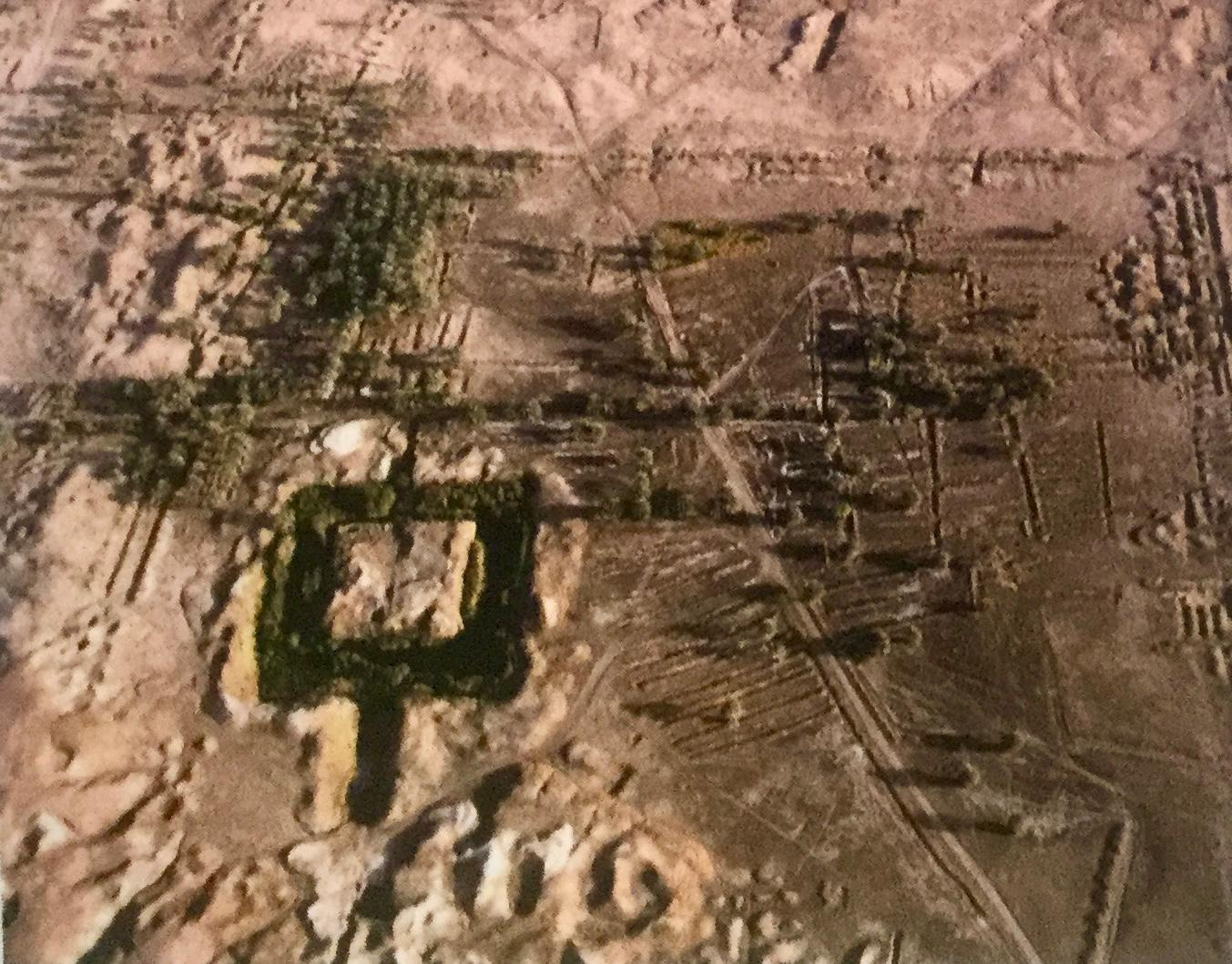 An aerial photograph of an ancient Mesopotamian city mound, its ruined walls and surrounding fields seen from above.